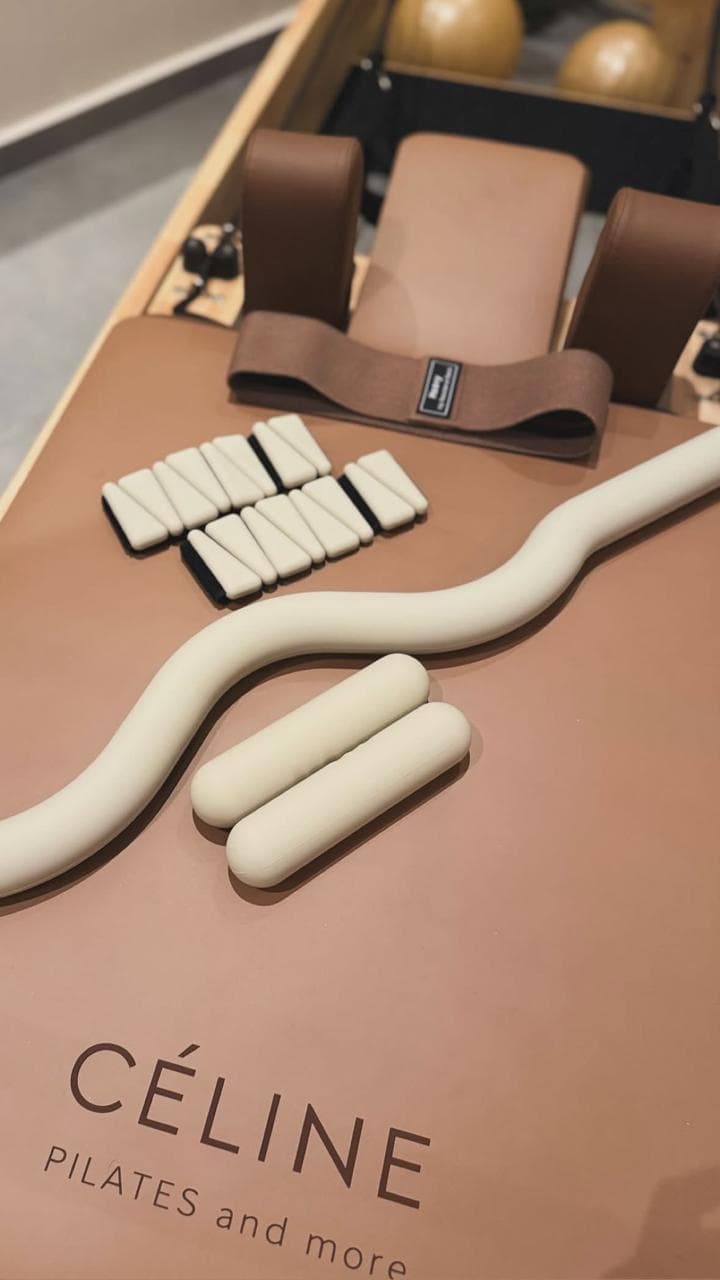 CÉLINE reformer carriage with resistance band, hand weights, and ankle weights arranged on the branded beige mat