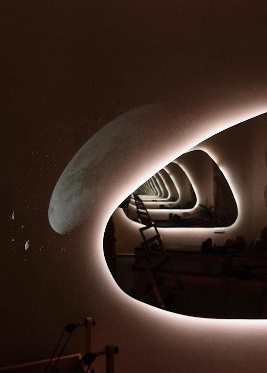 Backlit organic mirror in the CÉLINE studio with moonlight wall detail and reformer reflections